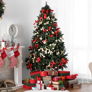 A decorated Christmas tree with red and gold bows is surrounded by various wrapped gifts. Nearby, a mantel displays candles, small figurines, and stockings.