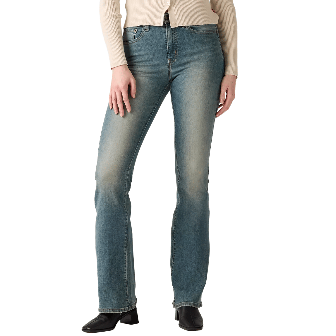 A person is wearing faded blue bootcut jeans paired with a beige ribbed sweater and black boots.