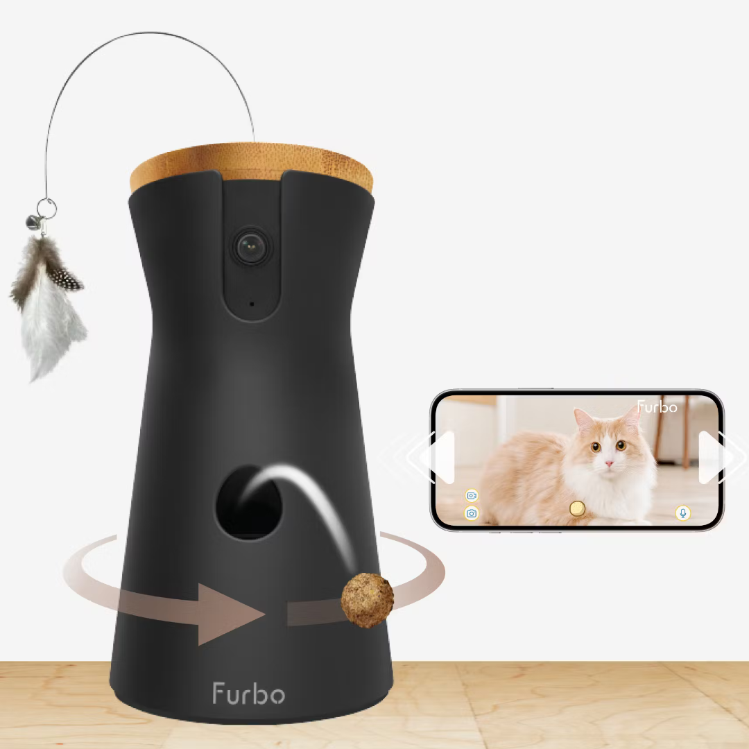 A black Furbo cat camera with treat dispenser and feather toy, shown alongside a smartphone displaying a cat.