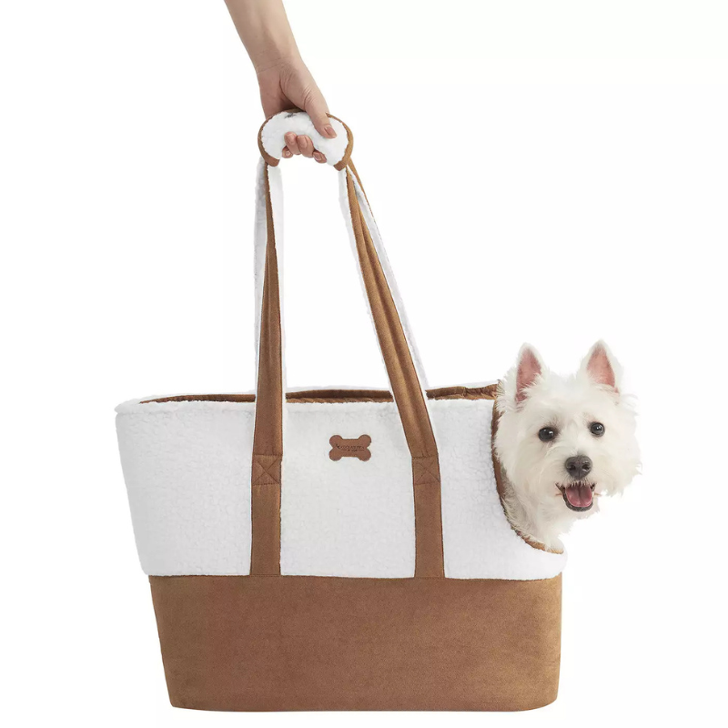 A brown and white pet carrier bag is shown with a small dog peeking out. The bag features a bone-shaped emblem and has long handles, suitable for carrying pets comfortably.
