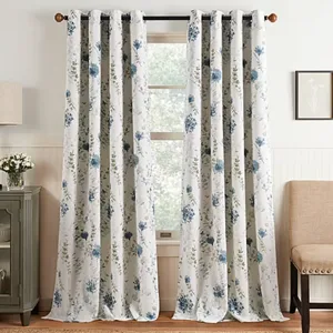 White curtain panels with blue floral patterns hanging on a black rod, set in a cozy room with a cabinet, lamp, and beige chair.