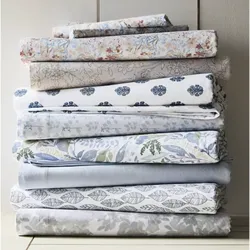 A stack of folded bedsheets featuring various floral and leaf patterns in soft pastel colors, including blue, gray, and beige tones.