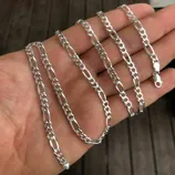 A silver Figaro chain is shown, featuring a pattern of three small circular links followed by one elongated oval link, with a lobster clasp for fastening.