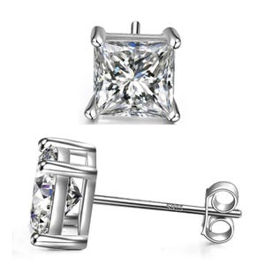 Silver square stud earrings feature a large, clear square-cut gemstone set in a four-prong setting. The post is marked with \“925,\“ indicating sterling silver.
