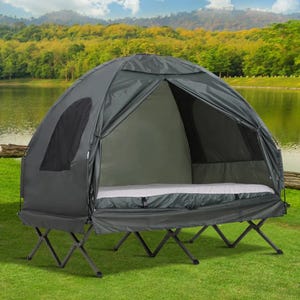 A black elevated camping tent with a built-in cot, zipped up, set against a natural background featuring a lake and trees.