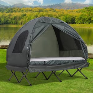 A black elevated camping tent with a built-in cot, zipped up, set against a natural background featuring a lake and trees.
