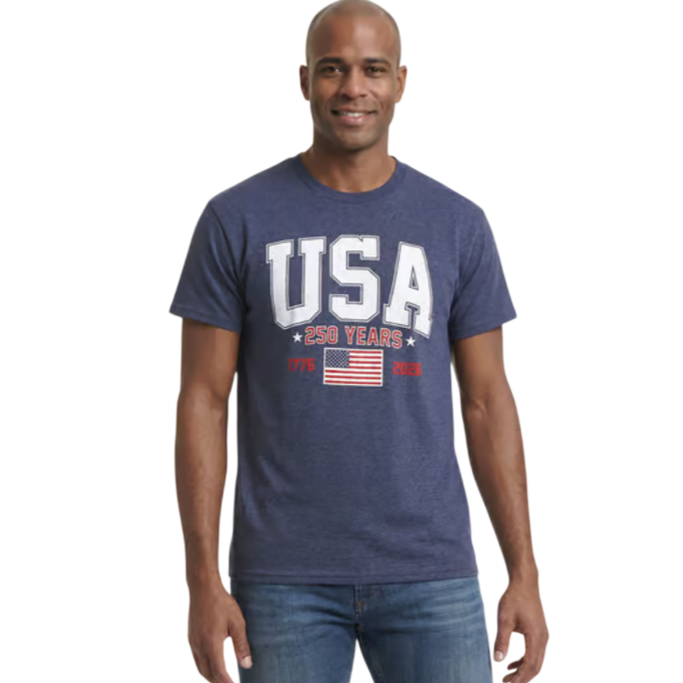 A man wears a blue T-shirt with \“USA 250 Years,\“ the dates 1776 and 2026, and an American flag design, paired with jeans.