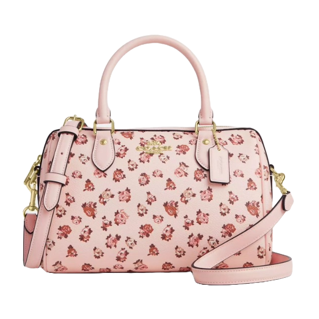 A pink Coach Outlet satchel featuring a floral print with small red and pink roses, gold-tone hardware, dual handles, and an adjustable strap.