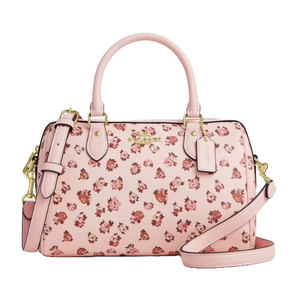 A pink Coach Outlet satchel featuring a floral print with small red and pink roses, gold-tone hardware, dual handles, and an adjustable strap.