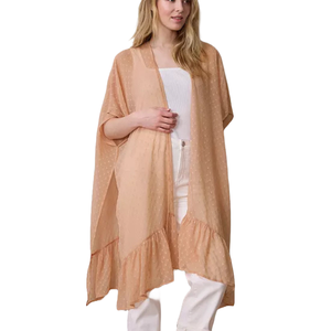 A woman is wearing a peach-colored, semi-sheer kimono cardigan with ruffled edges and white polka dots, over a white top and white pants.