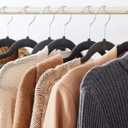 A set of hangers with a black velvet flocked surface, designed to prevent clothing from slipping. They hold various garments in neutral tones, such as knits and jackets.