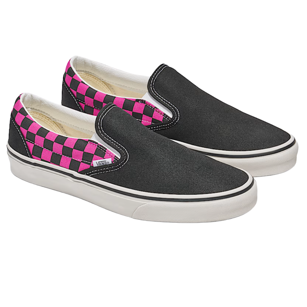 Black slip-on shoes with pink and black checkerboard pattern on the sides, featuring white soles and visible stitching.