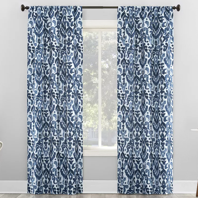 Blue and white patterned curtains with an abstract floral design hang on a black curtain rod in a bright room.
