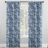 Blue and white patterned curtains with an abstract floral design hang on a black curtain rod in a bright room.