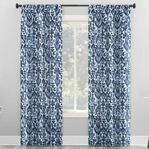 Blue and white patterned curtains with an abstract floral design hang on a black curtain rod in a bright room.