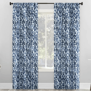 Blue and white patterned curtains with an abstract floral design hang on a black curtain rod in a bright room.