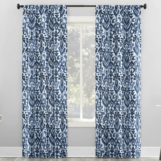 Blue and white patterned curtains with an abstract floral design hang on a black curtain rod in a bright room.