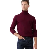 A man is wearing a burgundy turtleneck sweater paired with dark blue jeans against a neutral background.