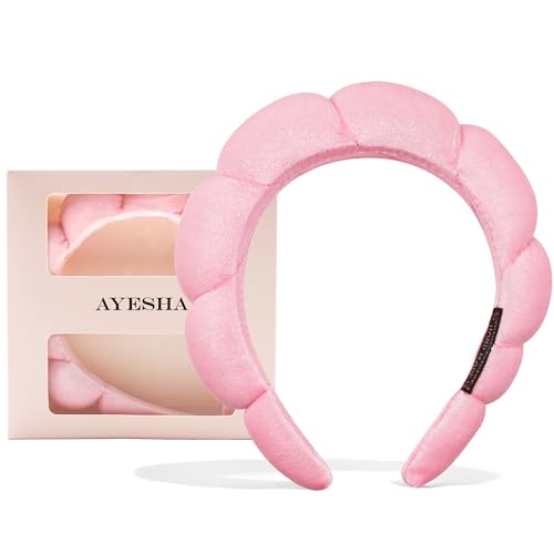 Pink, plush spa headband with a twist design at the top, displayed next to its packaging.