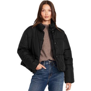 A woman is wearing a black Old Navy Quilted Puffer Jacket, featuring a high collar and button closure. She pairs it with a brown sweater and high-waisted blue jeans, creating a casual and cozy look.