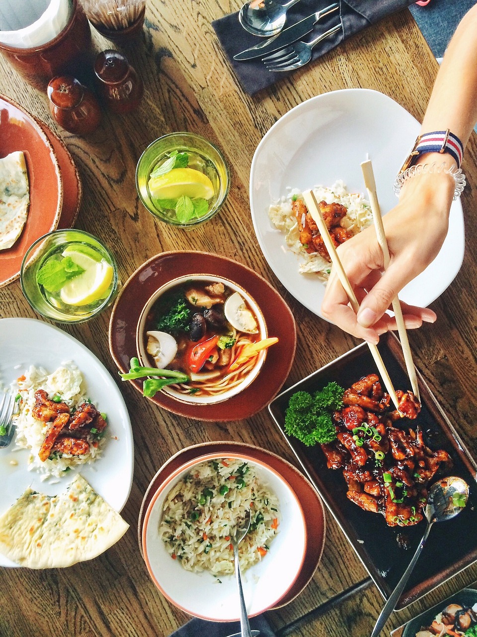 A variety of Asian dishes on a table, including noodles, rice, and chicken with chopsticks in use.