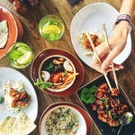 A variety of Asian dishes on a table, including noodles, rice, and chicken with chopsticks in use.