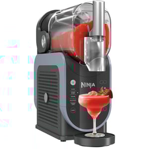 The Refurbished Ninja SLUSHi is a countertop slush maker with a sleek black and gray design, featuring a transparent container filled with red slush. It dispenses slush into a glass below, with controls on the front panel for easy operation.