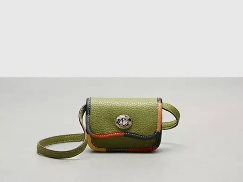 A green textured shoulder bag with an orange and black trim and a circular metallic clasp.