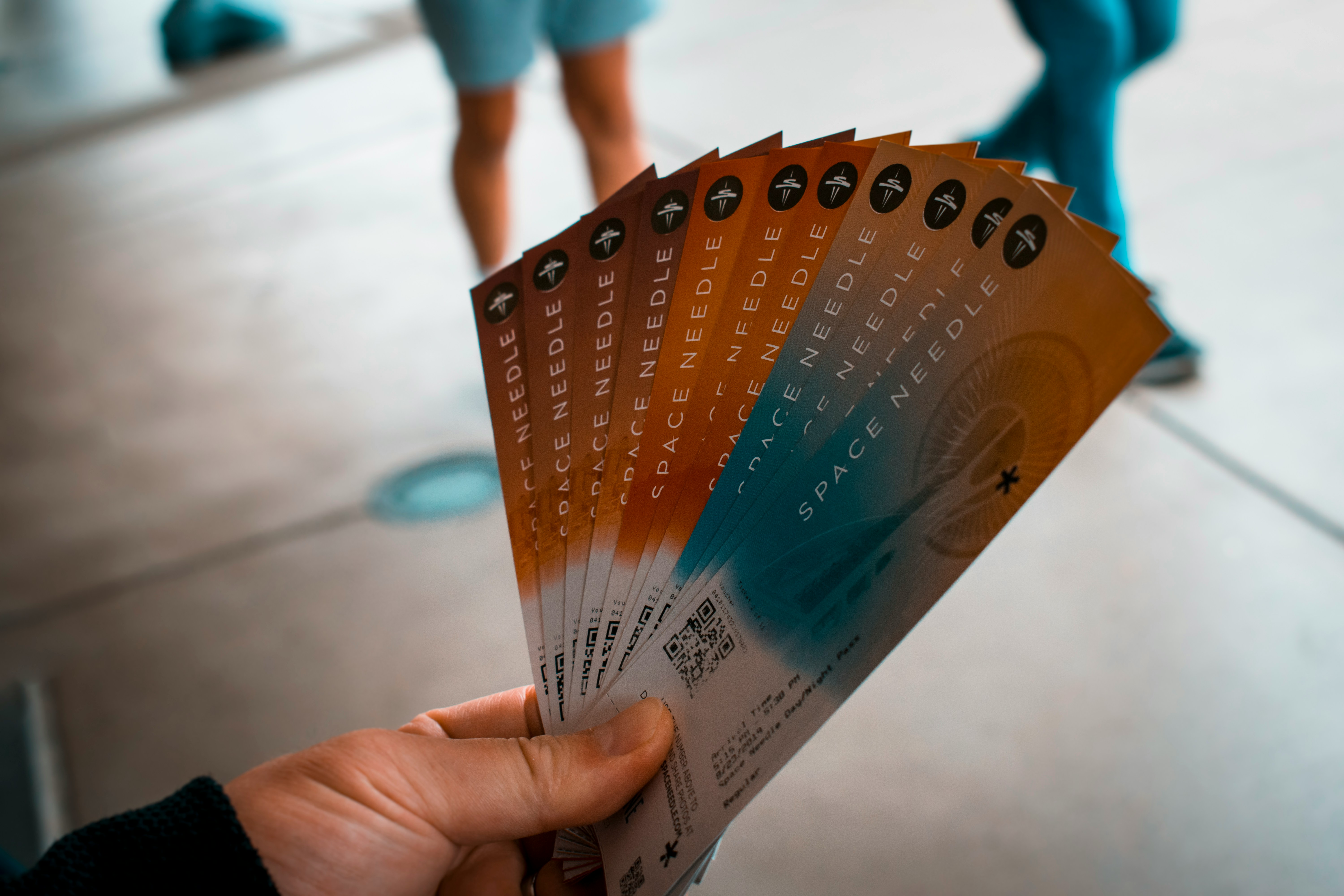 A hand is holding a fan of tickets for the Space Needle attraction.