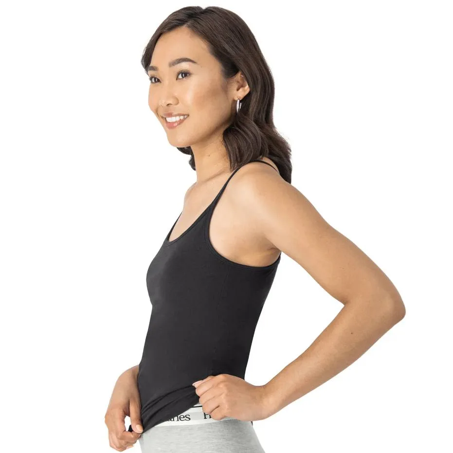 A woman models a black Hanes Shelf Bra Cami featuring thin straps and an integrated shelf bra, paired with light gray bottoms. It's designed for comfort and ease, suitable for layering or wearing alone.