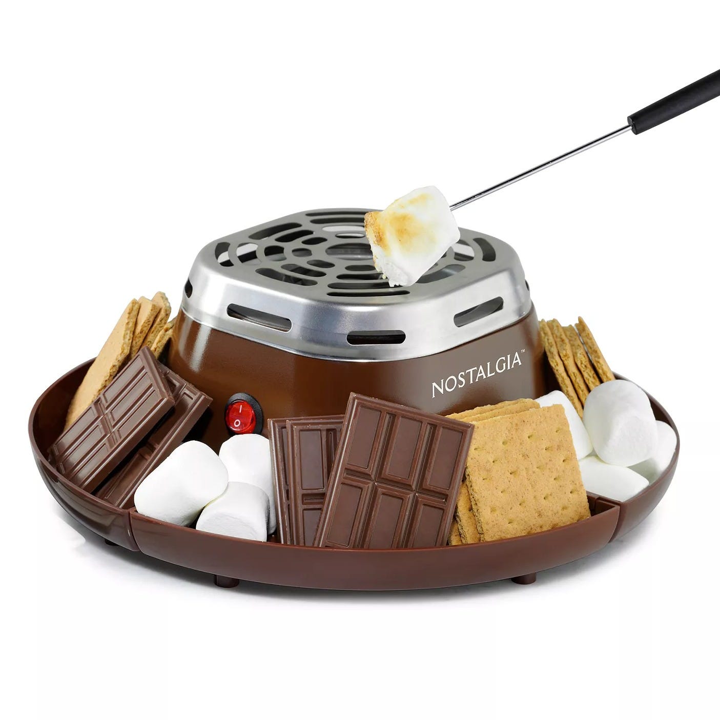 Electric s'mores maker by Nostalgia featuring a roasting station with a skewer, surrounded by marshmallows, chocolate pieces, and graham crackers.