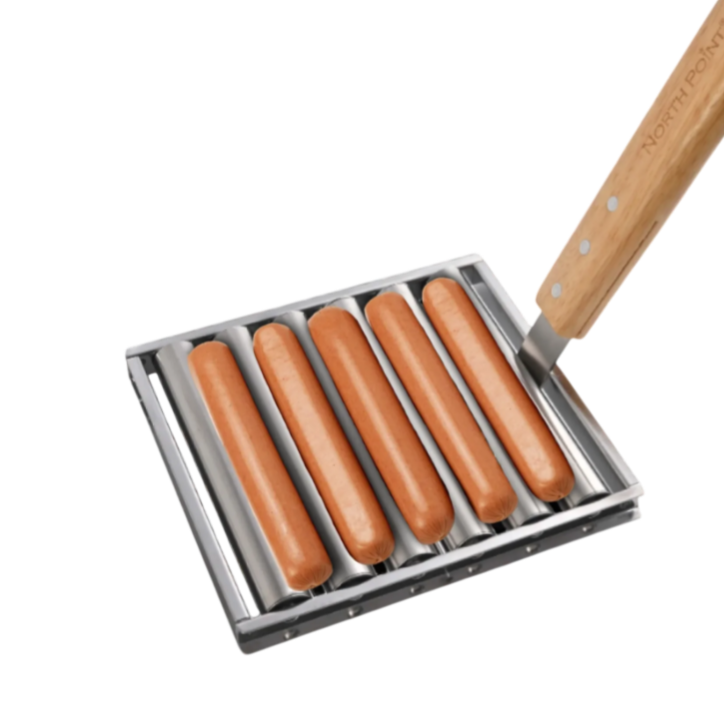 A hot dog grilling tray holds five sausages over a flame, featuring a wooden handle marked with \“North Point.\“