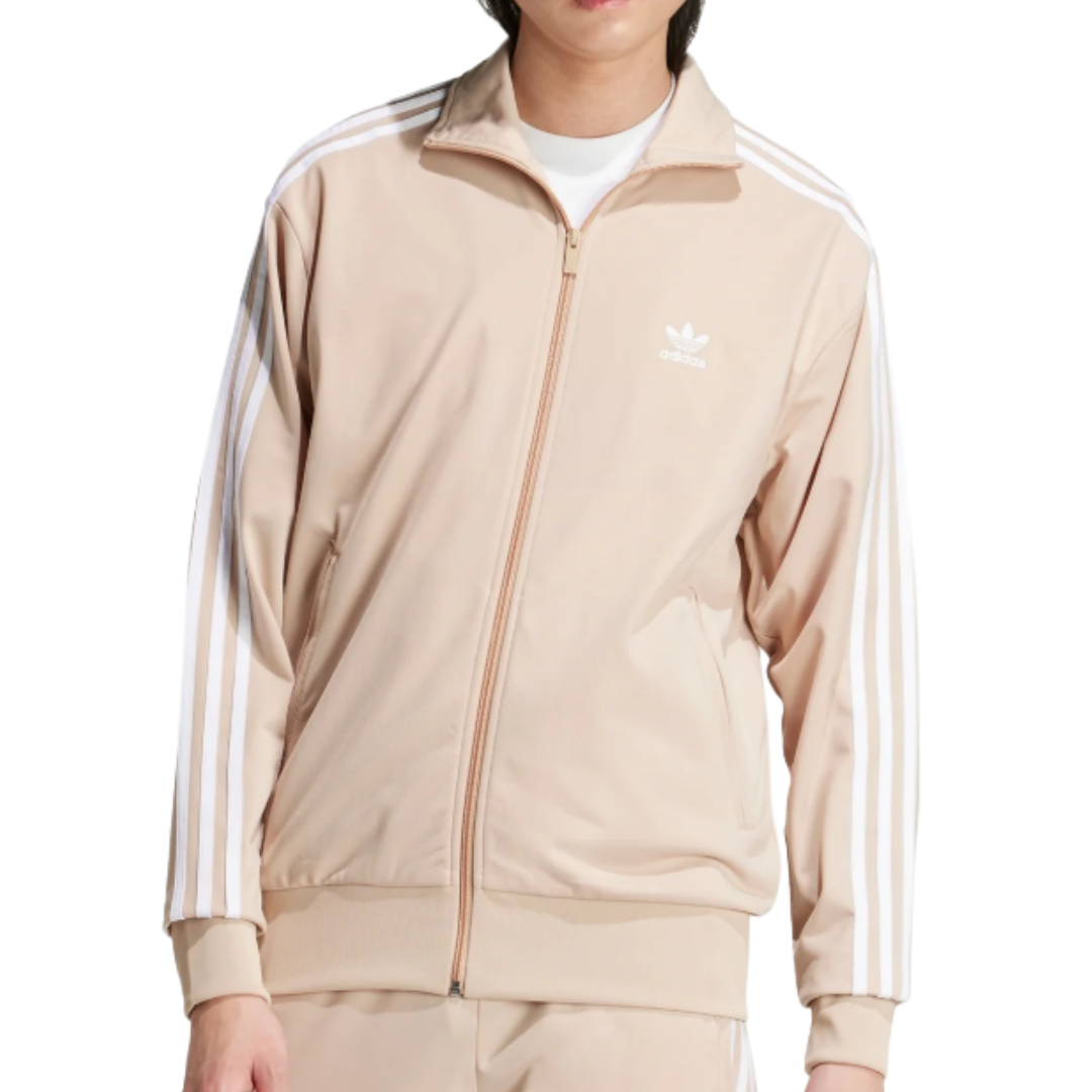 A beige Adidas track jacket featuring white stripes on the sleeves and the Adidas logo on the chest, worn over a white shirt.