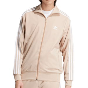 A beige Adidas track jacket featuring white stripes on the sleeves and the Adidas logo on the chest, worn over a white shirt.
