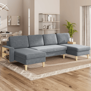 Gray L-shaped sectional sofa with built-in side tables and wooden legs, set in a modern living room with a light rug, hardwood floors, and minimalist decor including a bookshelf and potted plant.