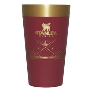 A red Stanley beer pint with a gold rim, featuring the brand's logo and decorative mountain-style graphics.