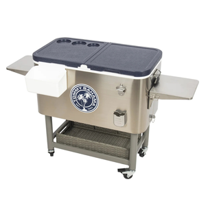 The Tommy Bahama 100-Qt. Cooler is a stainless steel cooler on wheels, featuring a logo, bottle opener, cap catcher, side shelves, and a storage shelf beneath. It has a durable, insulated design with a top lid that includes cup holders.