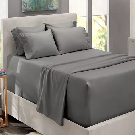 A neatly made bed with gray sheets, including pillowcases, a fitted sheet, and a flat sheet, against a neutral-colored headboard.