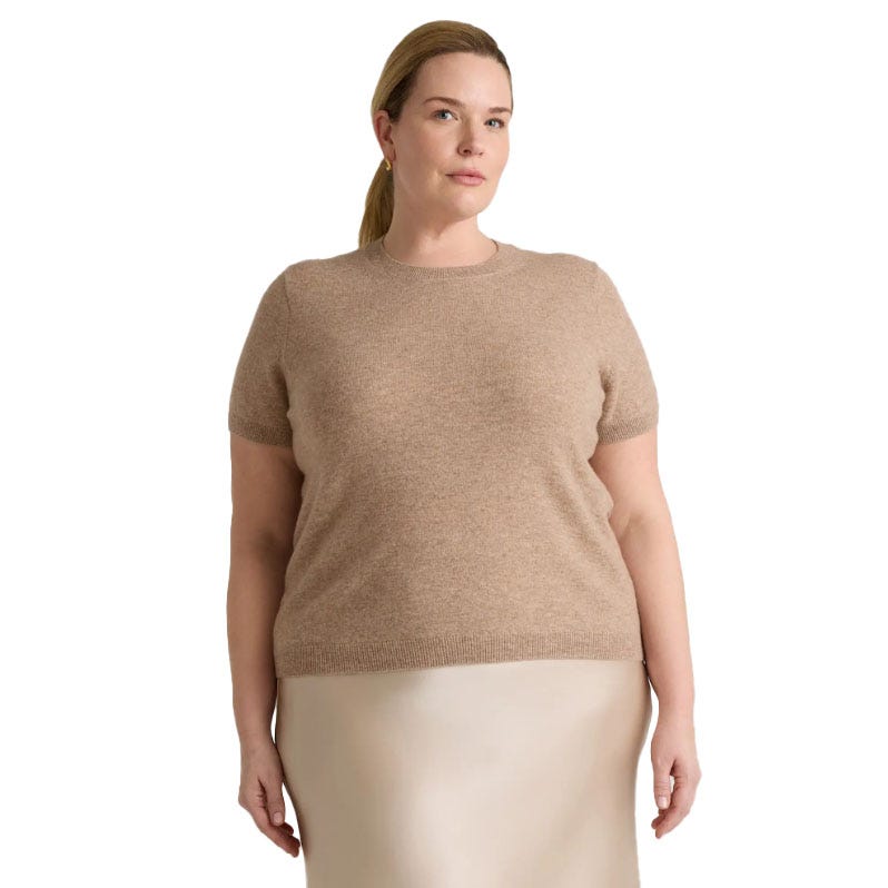A woman wears a beige cashmere tee with short sleeves and a round neckline, paired with a light-colored skirt.