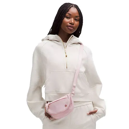 A person wearing a cream hooded sweatshirt with a front pocket zipper is accessorized with a light pink crossbody bag.
