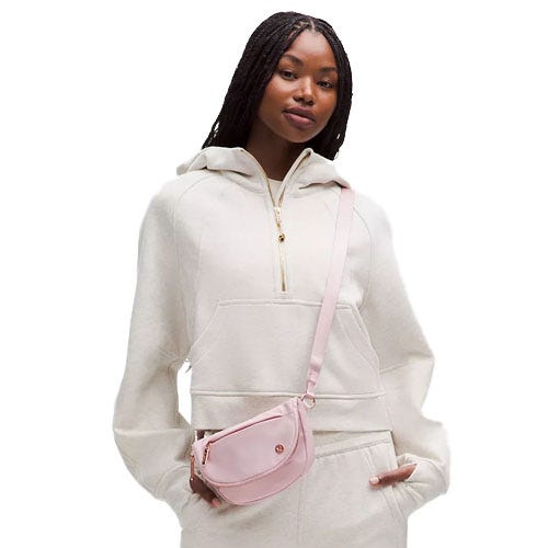 A person wearing a cream hooded sweatshirt with a front pocket zipper is accessorized with a light pink crossbody bag.