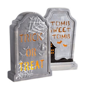 Two Halloween-themed decorative tombstones with \“Trick or Treat\“ and \“Tombs Sweet Tombs\“ inscribed.