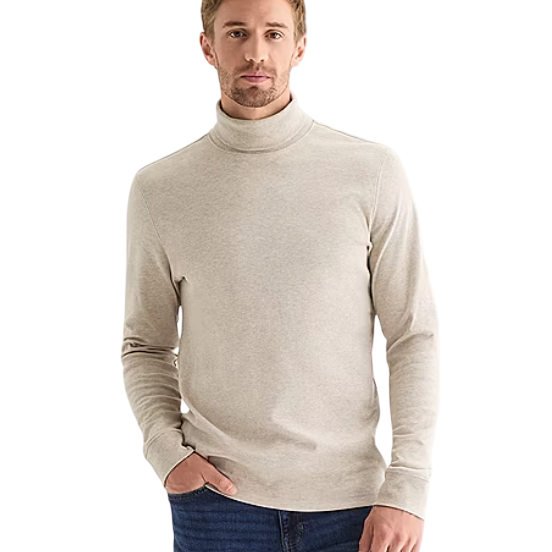 A man is wearing a beige turtleneck sweater paired with blue jeans.