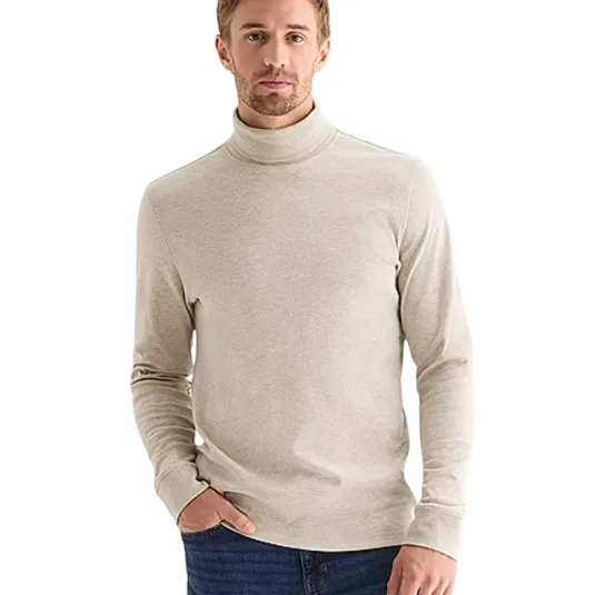 A man is wearing a beige turtleneck sweater paired with blue jeans.