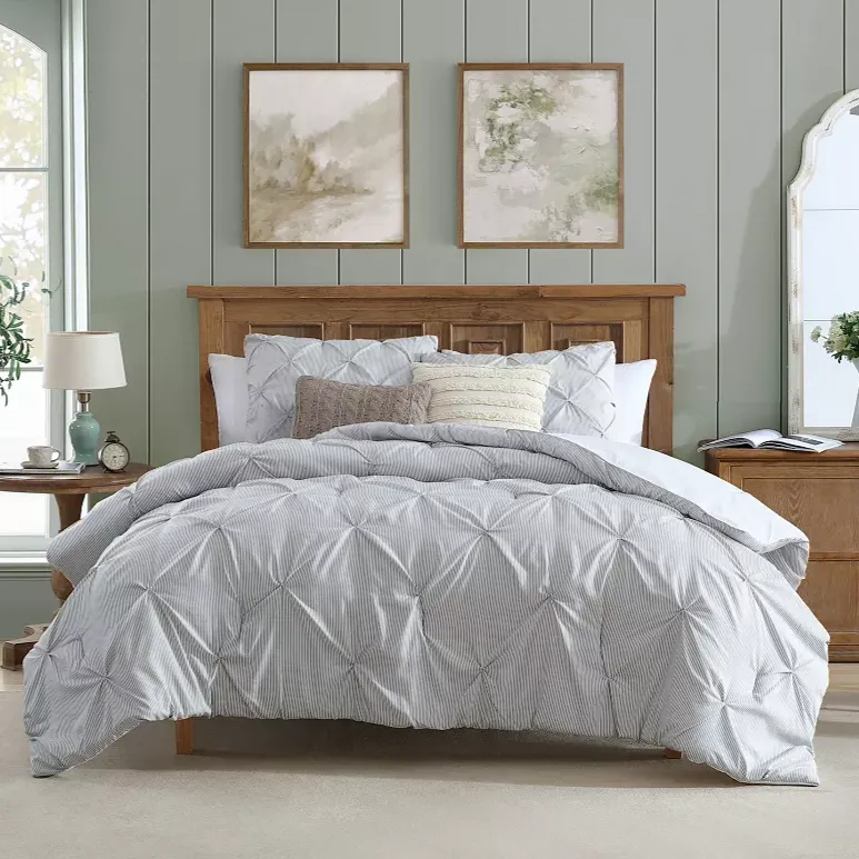 Bedroom featuring a cozy bed with a light gray, striped comforter and decorative pillows, wooden headboard and side tables, two landscape paintings, a round lamp, and a large mirror, creating a serene and inviting atmosphere.