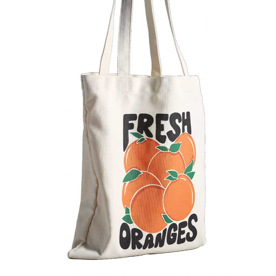 A canvas tote bag with \“Fresh Oranges\“ printed in bold black letters, featuring an illustration of multiple oranges with green leaves.