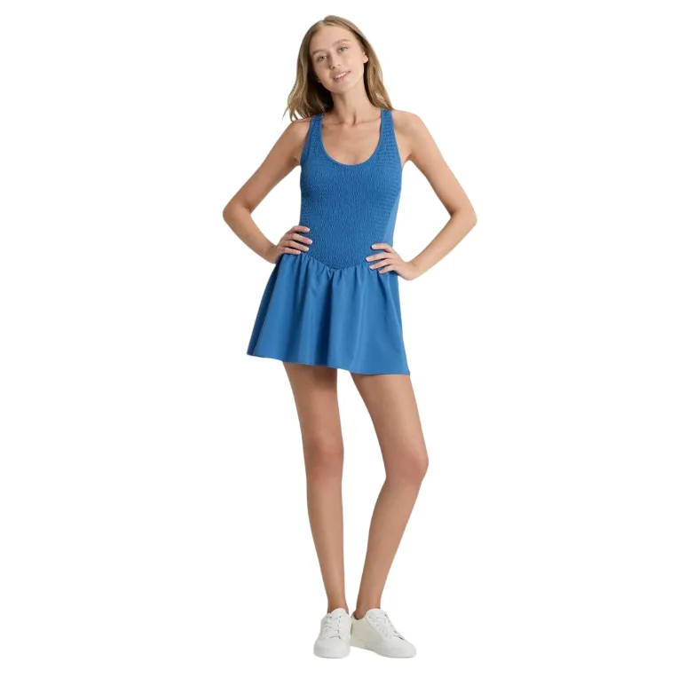 A woman is wearing a blue sleeveless mini dress with a fitted top and flared skirt, paired with white sneakers.