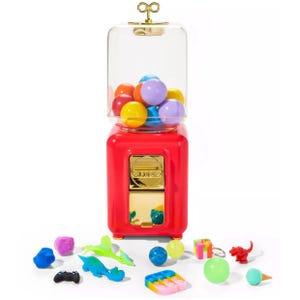 A toy vending machine with colorful balls and various small toys, including a dinosaur, game controller, ice cream cone, and gift box, displayed around it.