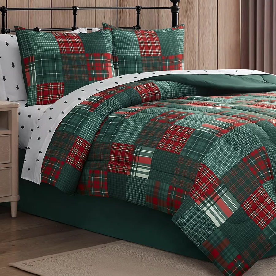 A bed features a patchwork quilt and matching pillow shams with red and green plaid patterns, complemented by white sheets with small black tree designs. The setup includes a black metal headboard and a wooden nightstand.