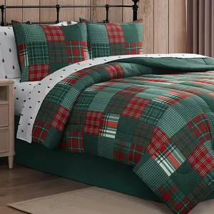 A bed features a patchwork quilt and matching pillow shams with red and green plaid patterns, complemented by white sheets with small black tree designs. The setup includes a black metal headboard and a wooden nightstand.